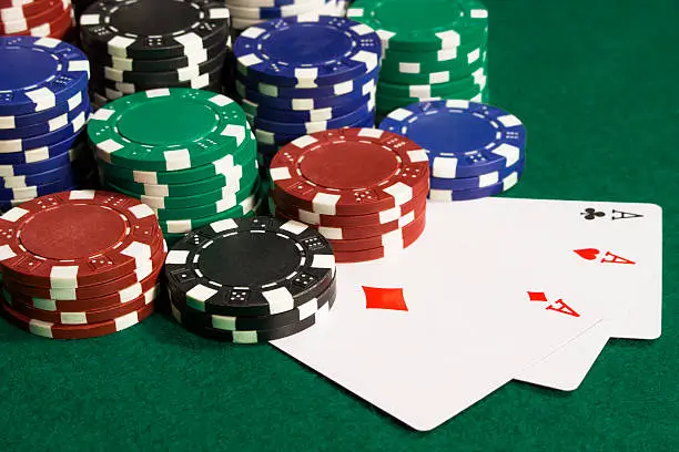 um close de um jogo de pôquer em andamento com pilhas de fichas multicoloridas e dois ases virados para cima em uma mesa verde, indicando uma mão forte.
